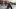 Drei Personen sitzen mit VR-Brillen und Kopfhörern auf grauen Würfeln in einem Raum mit Stühlen und Tischen im Hintergrund.